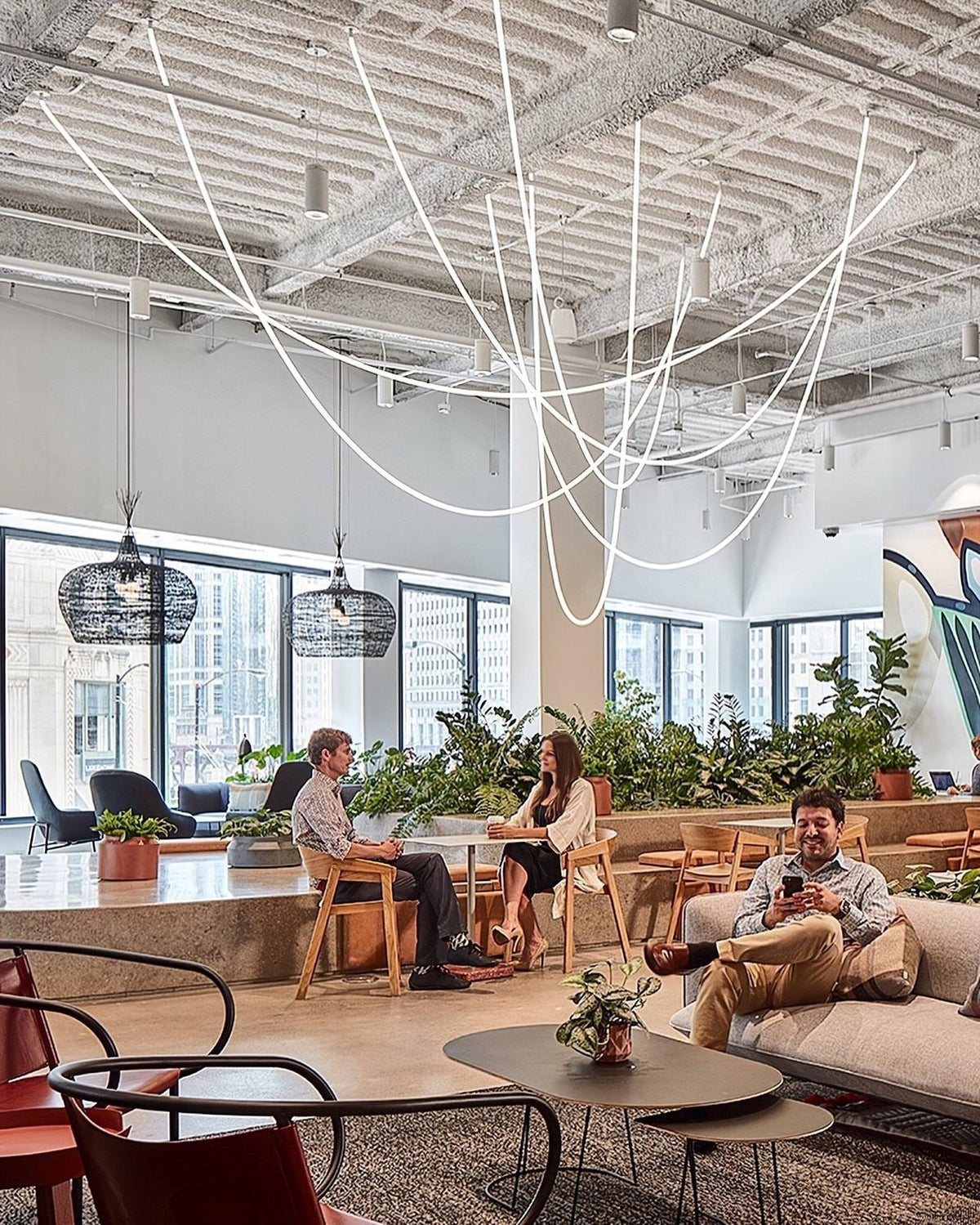 Thin Clérachic rope pendants sweeping across a high ceiling above a lounge with a low table, plants and sofa seating.