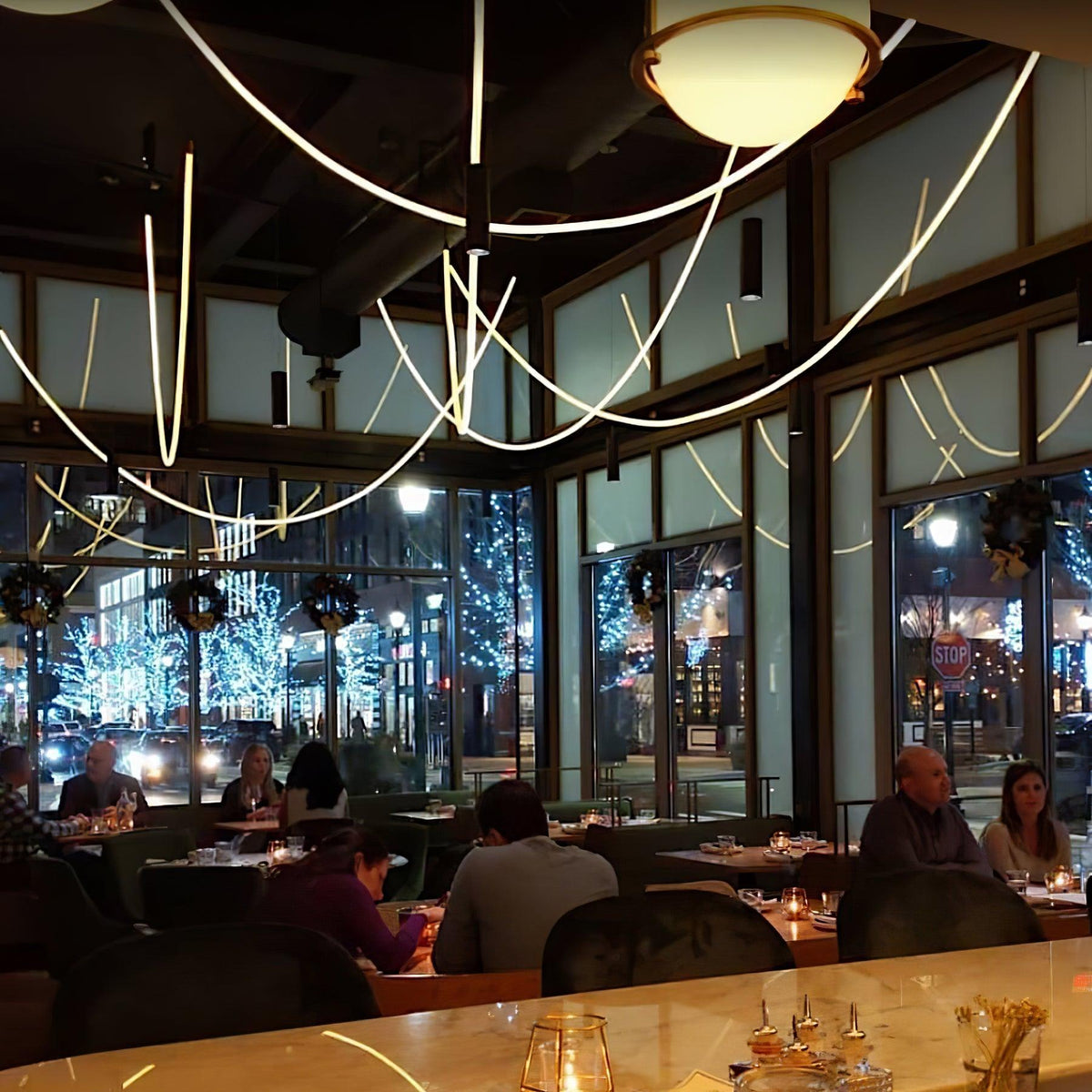 Clérachic LED rope pendants looping across a dark glazed restaurant at night, above diners and a glowing dome light.