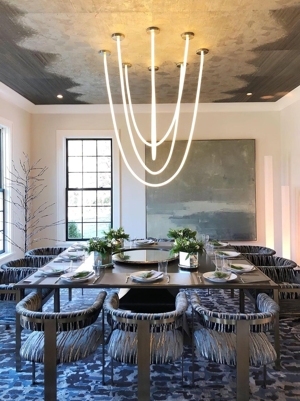 Five Clérachic LED rope pendants forming a glowing cluster above a dining table with patterned chairs and a green-grey painting.