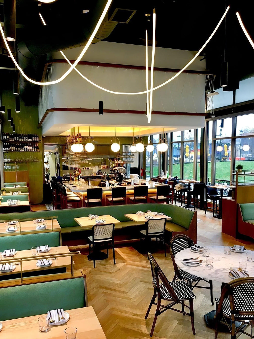 Clérachic LED rope pendants looping high above a green-banquette restaurant, seen in a taller, narrower view.