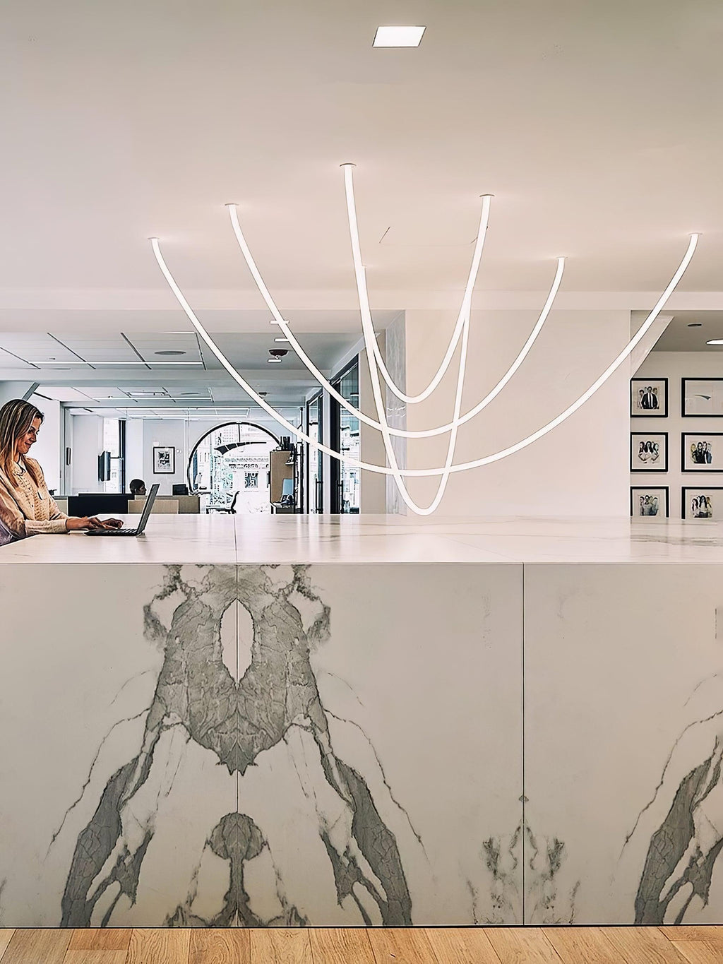 A cluster of Clérachic LED rope pendants over a marble-fronted counter, with a woman working at a laptop and framed prints behind.