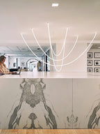 A cluster of Clérachic LED rope pendants over a marble-fronted counter, with a woman working at a laptop and framed prints behind.