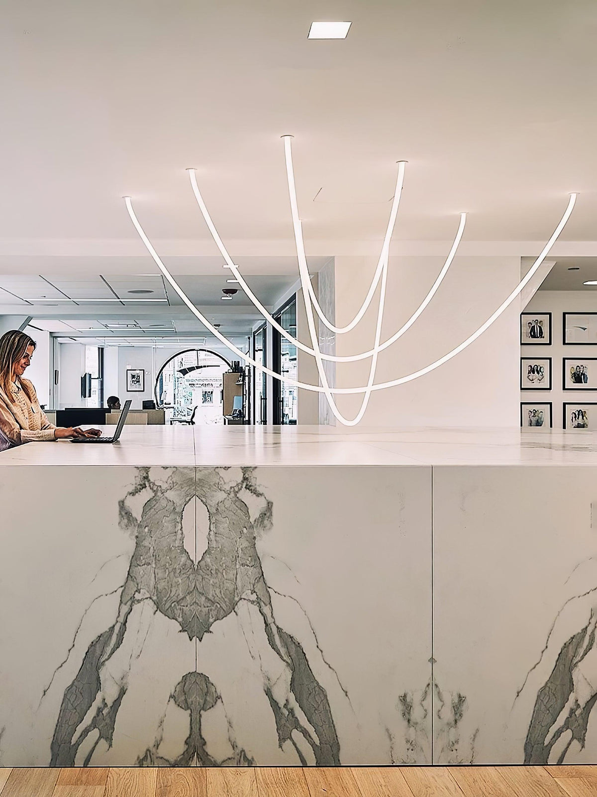 A cluster of Clérachic LED rope pendants over a marble-fronted counter, with a woman working at a laptop and framed prints behind.