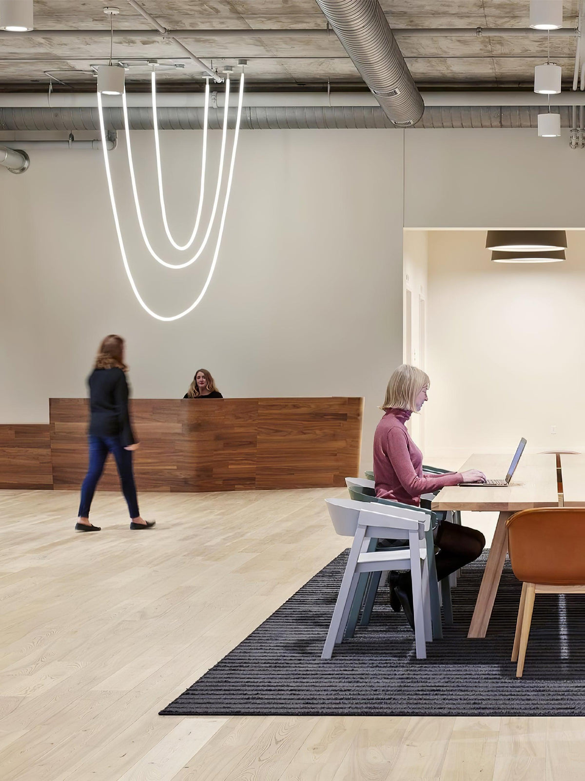 Clérachic LED rope pendants dropping in tall loops in an open-plan office, with a reception desk and people at tables below.
