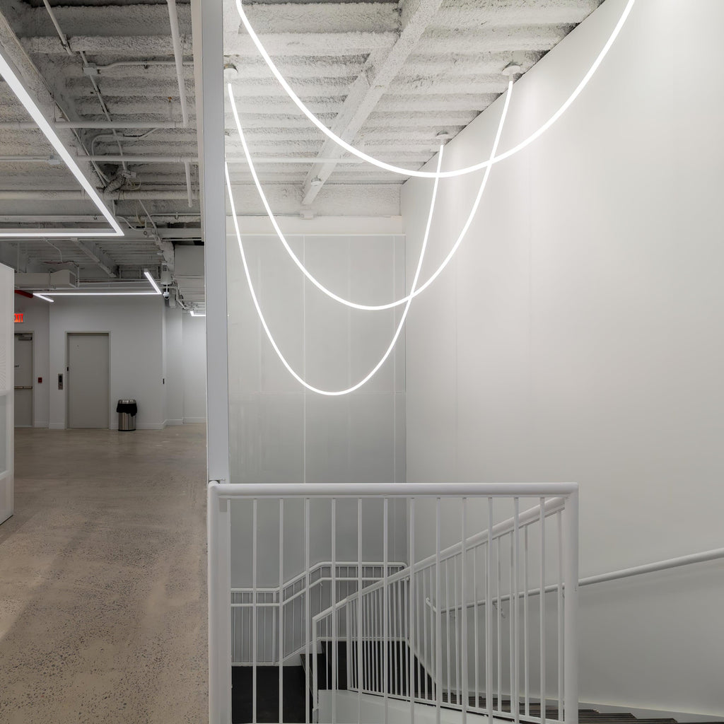 Clérachic LED rope pendants forming glowing loops over a white stairwell with a white railing and a bare concrete floor.