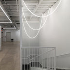 Clérachic LED rope pendants forming glowing loops over a white stairwell with a white railing and a bare concrete floor.