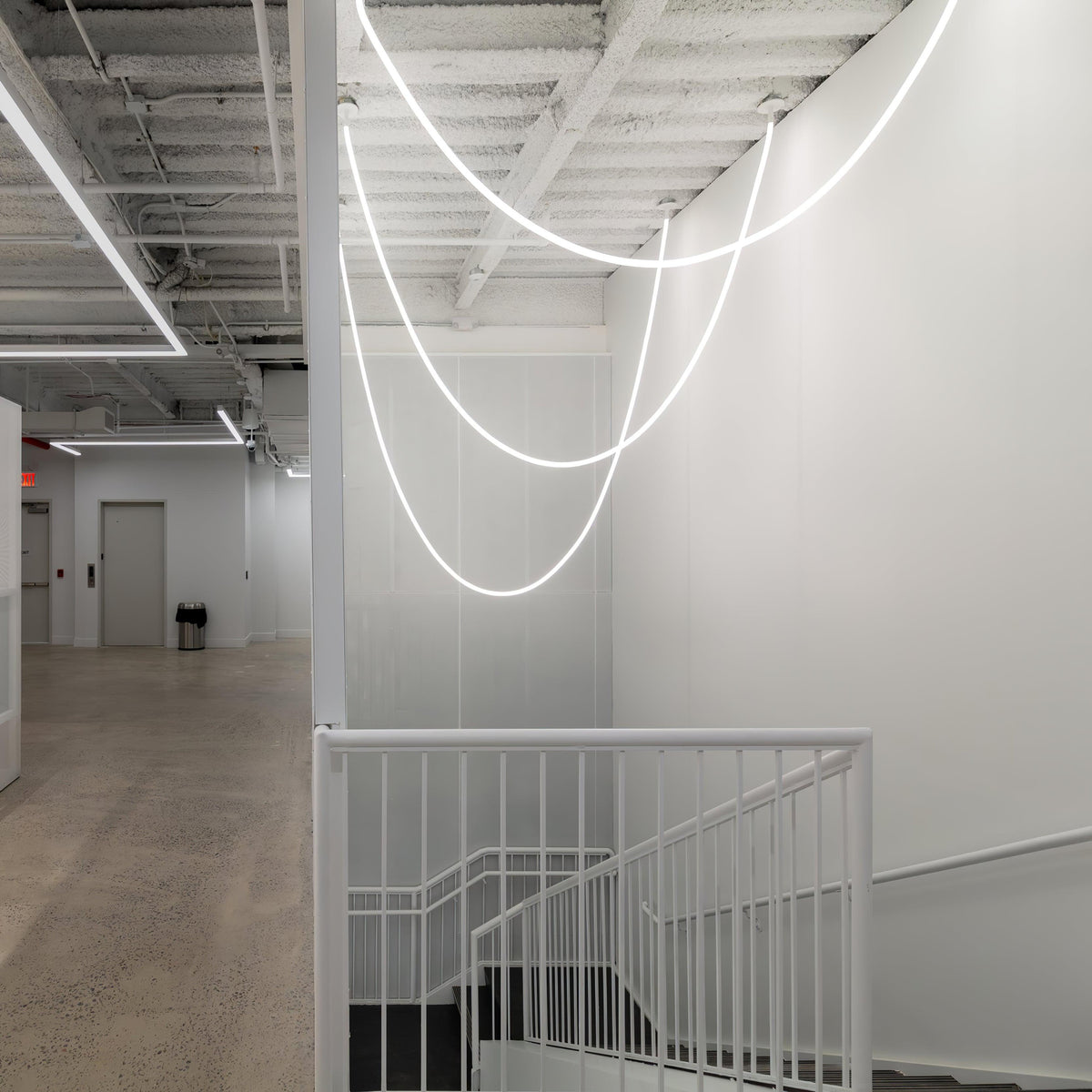 Clérachic LED rope pendants forming glowing loops over a white stairwell with a white railing and a bare concrete floor.