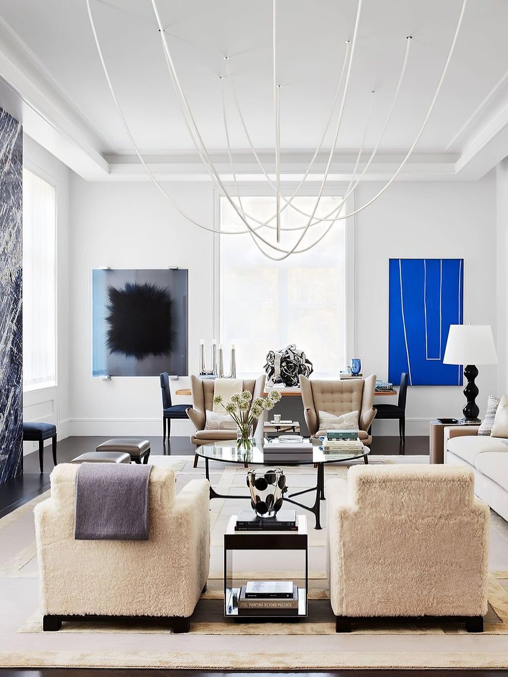 Pale Clérachic rope pendants curving across a white ceiling above a living room with fluffy armchairs and a blue artwork.