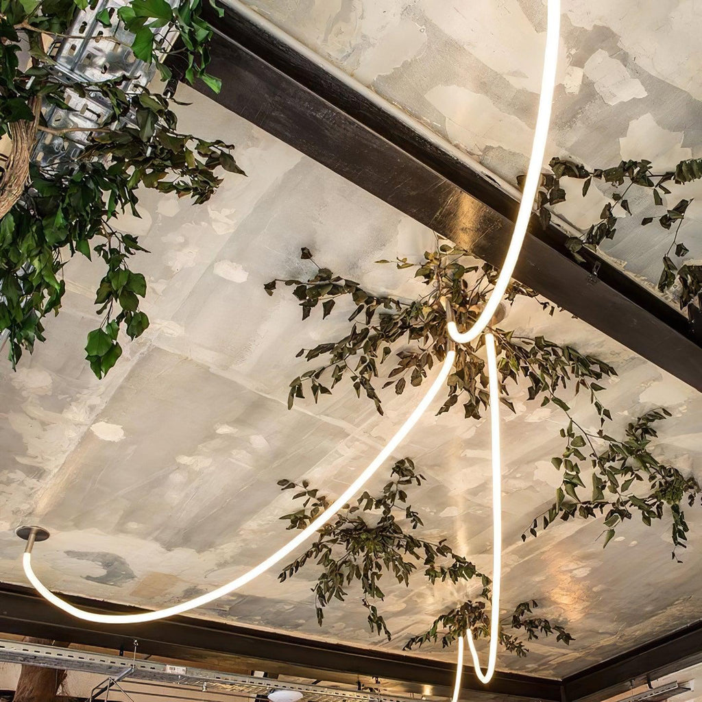 A Clérachic LED rope pendant sweeping across a ceiling beam in a close view, with tree leaves and a mirrored panel ceiling.