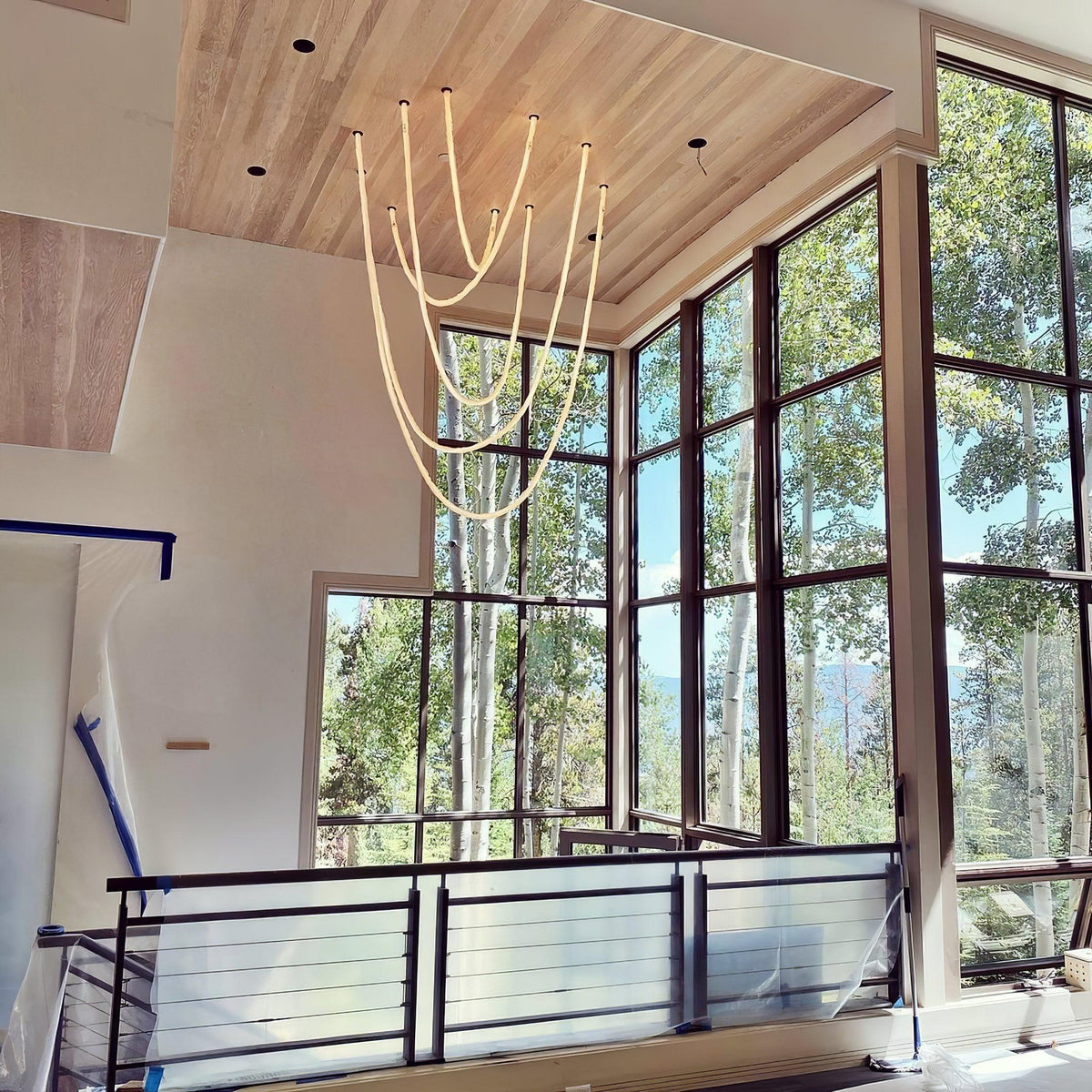 Clérachic LED rope pendants clustered in a tall room with a timber ceiling, below large windows with birch trees outside.
