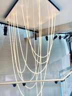 Many long Clérachic LED rope pendants dropping through a white square opening above a stairwell with a glass balustrade.