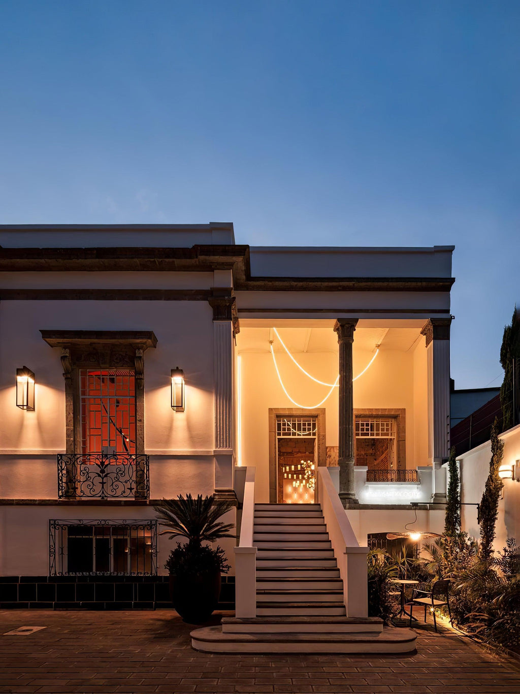 A Clérachic LED rope pendant glowing in the porch of a white house at dusk, with warm lights and steps at the front.