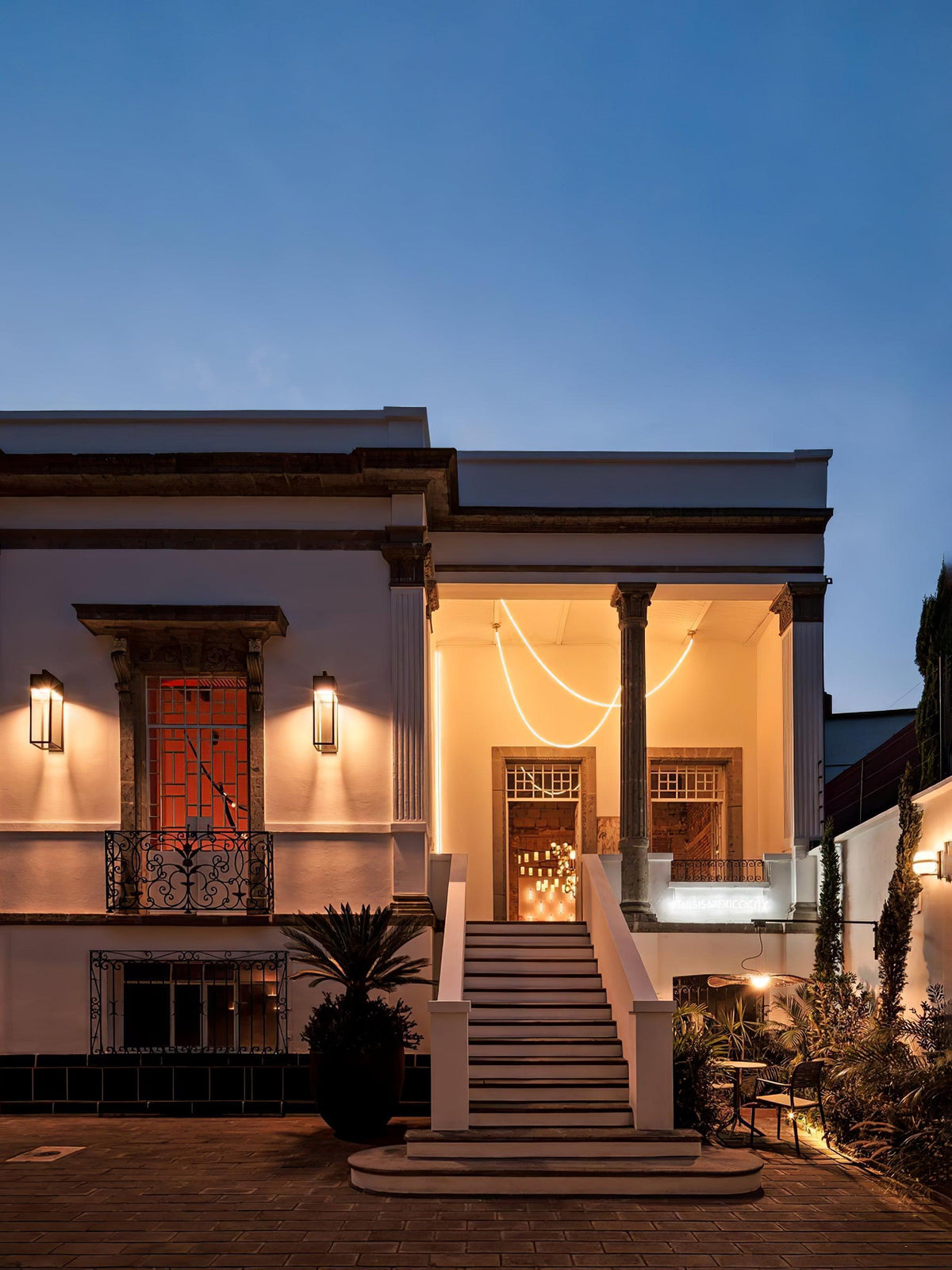 A Clérachic LED rope pendant glowing in the porch of a white house at dusk, with warm lights and steps at the front.