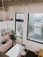 Long Clérachic rope pendants draped from a high ceiling in a pink-white kitchen with big windows and houseplants.