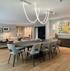 Clérachic LED rope pendants in loops above a long dark dining table with grey chairs and a bright abstract painting behind.