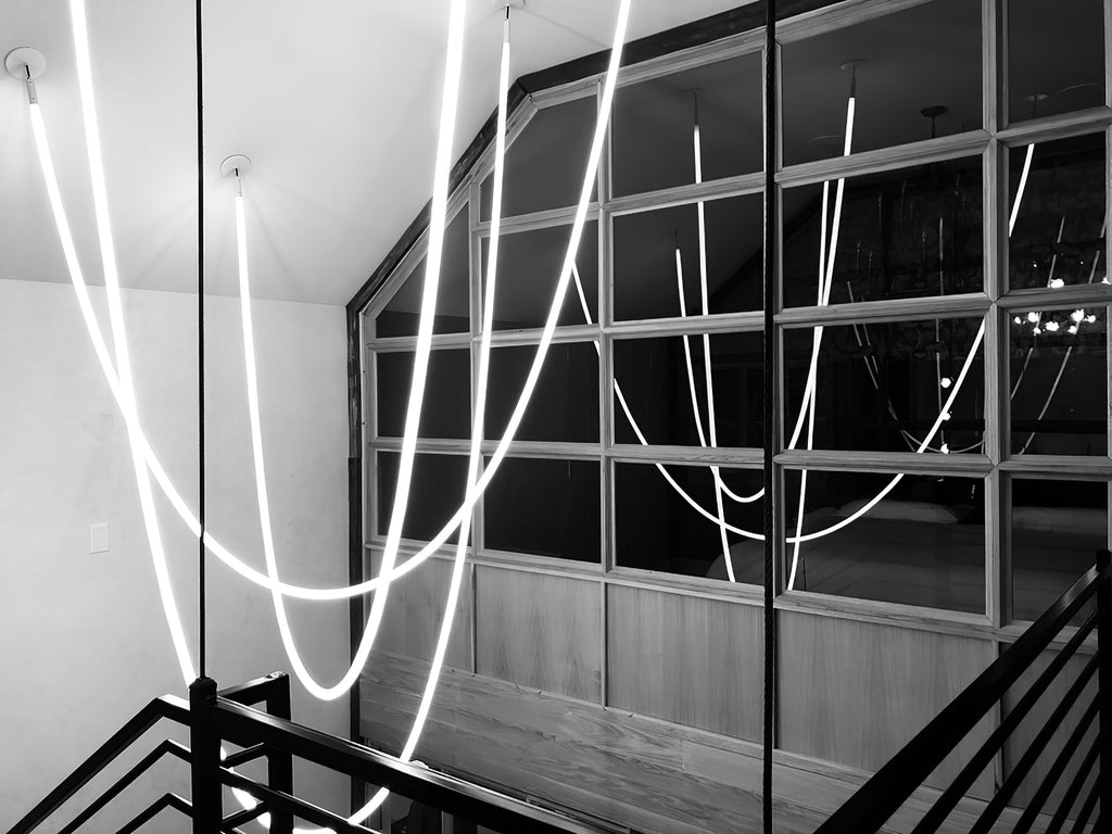 A black-and-white view of Clérachic LED rope pendants looping beside a dark railing and a large paned window.