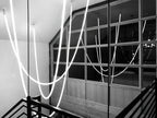 A black-and-white view of Clérachic LED rope pendants looping beside a dark railing and a large paned window.