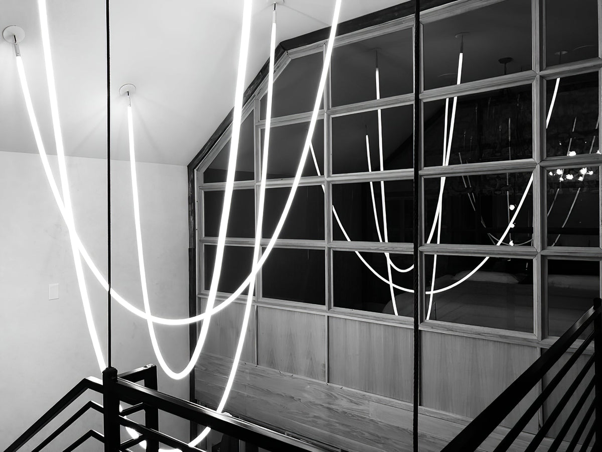A black-and-white view of Clérachic LED rope pendants looping beside a dark railing and a large paned window.