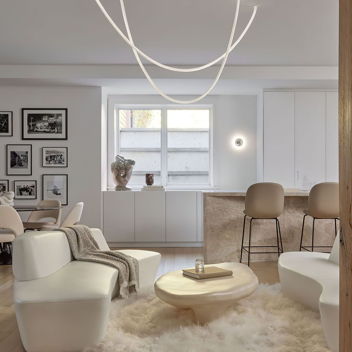 Soft loops of Clérachic LED rope pendants above a cream living room with a pale sofa, a shaggy rug and a round side table.