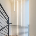 Several Clérachic LED rope pendants dropping in straight lines beside a dark stair railing in a tall white stairwell.