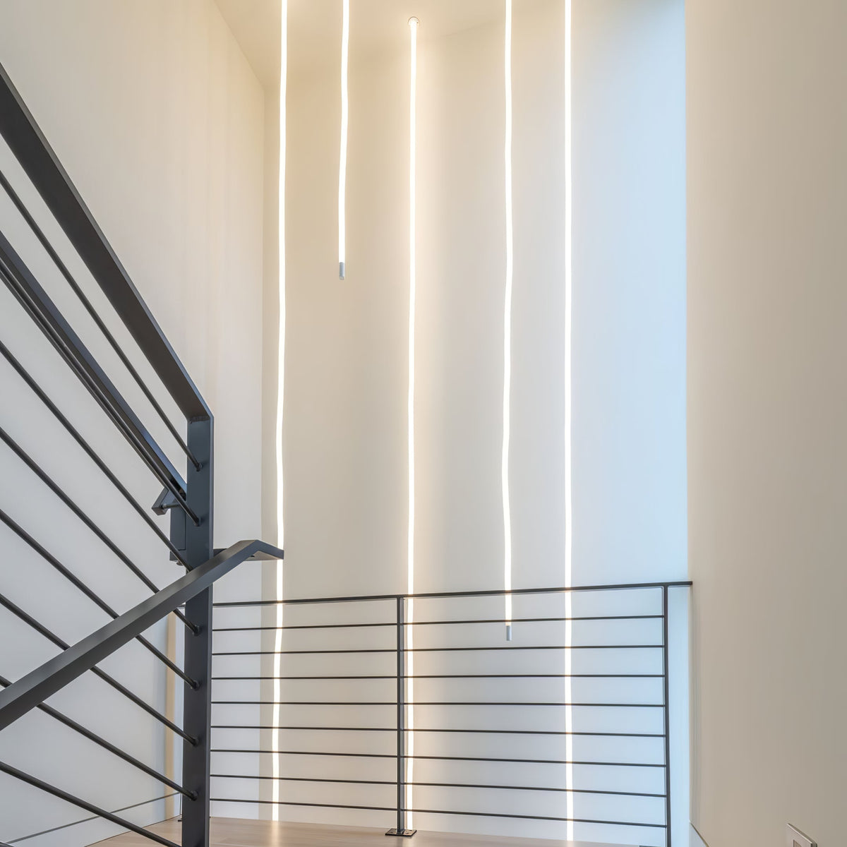 Several Clérachic LED rope pendants dropping in straight lines beside a dark stair railing in a tall white stairwell.