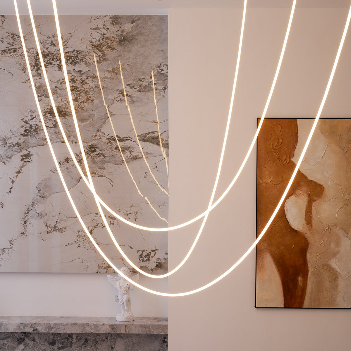 Close view of Clérachic LED rope pendants looping in front of a stone-patterned wall and a rust-coloured painting.
