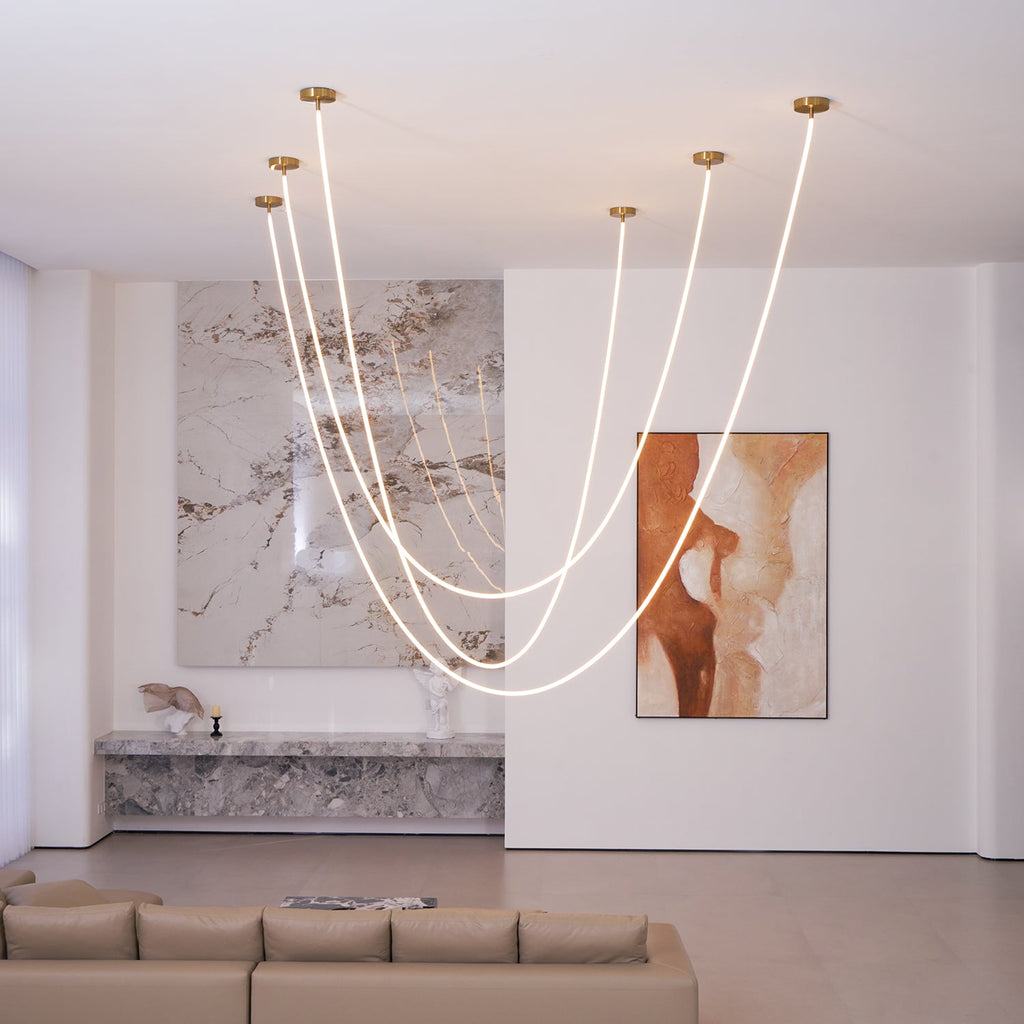 A group of Clérachic LED rope pendants from the ceiling, looping before a stone wall, a painting and a long grey sofa.