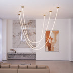 A group of Clérachic LED rope pendants from the ceiling, looping before a stone wall, a painting and a long grey sofa.