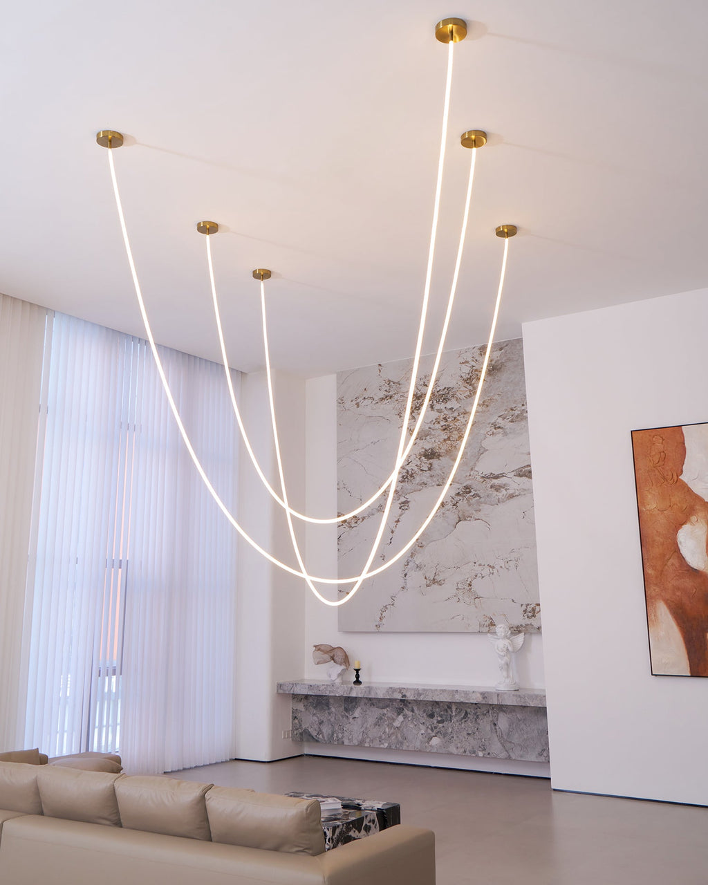 Tall view of Clérachic LED rope pendants looping in front of sheer curtains and a marble wall, with a sofa at the bottom.