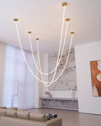 Tall view of Clérachic LED rope pendants looping in front of sheer curtains and a marble wall, with a sofa at the bottom.