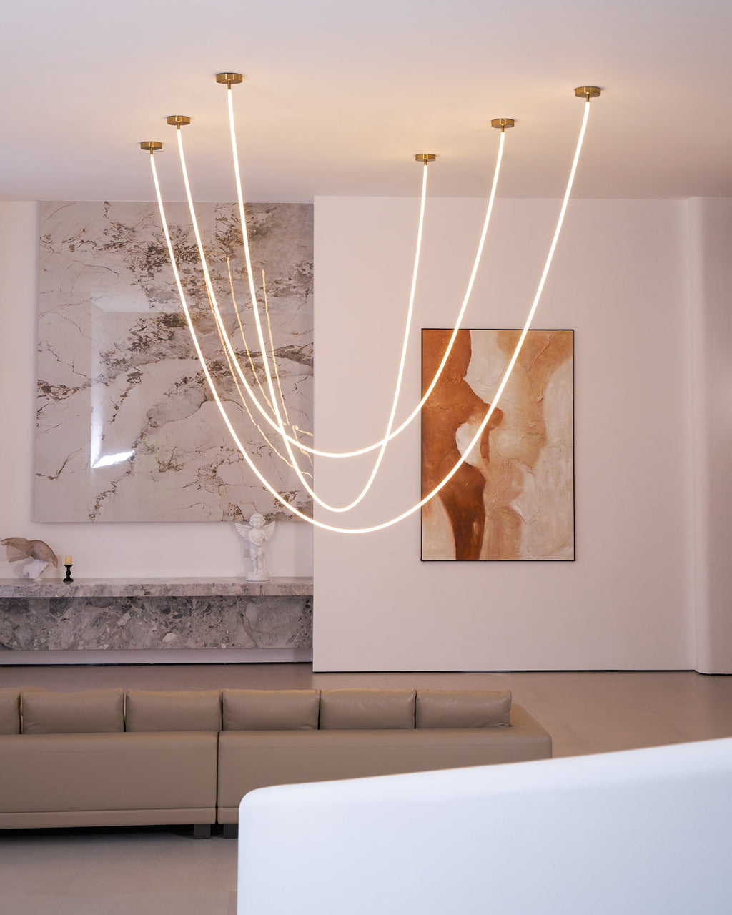 Clérachic LED rope pendants in different loop depths, in front of a marble wall and a painting, with a sofa and a white bench below.
