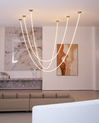 Clérachic LED rope pendants in different loop depths, in front of a marble wall and a painting, with a sofa and a white bench below.