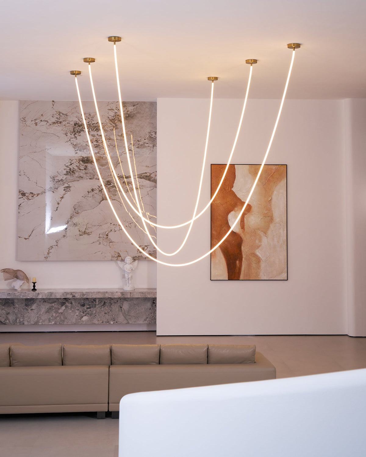 Clérachic LED rope pendants in different loop depths, in front of a marble wall and a painting, with a sofa and a white bench below.