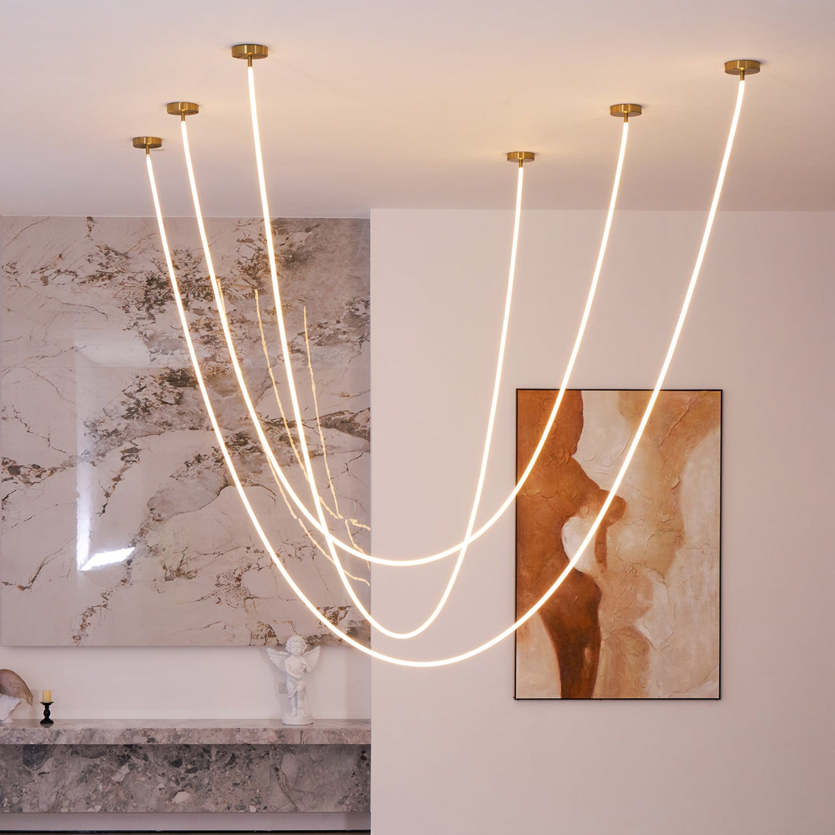 A wider group of Clérachic LED rope pendants glowing before a marble wall and a rust-and-cream painting, above a grey marble shelf.