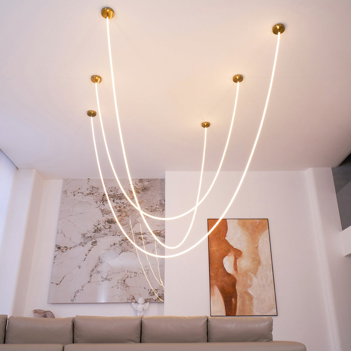 Clérachic LED rope pendants with gold-toned plates set at different heights, in a room with a taupe sofa and a marble feature wall.