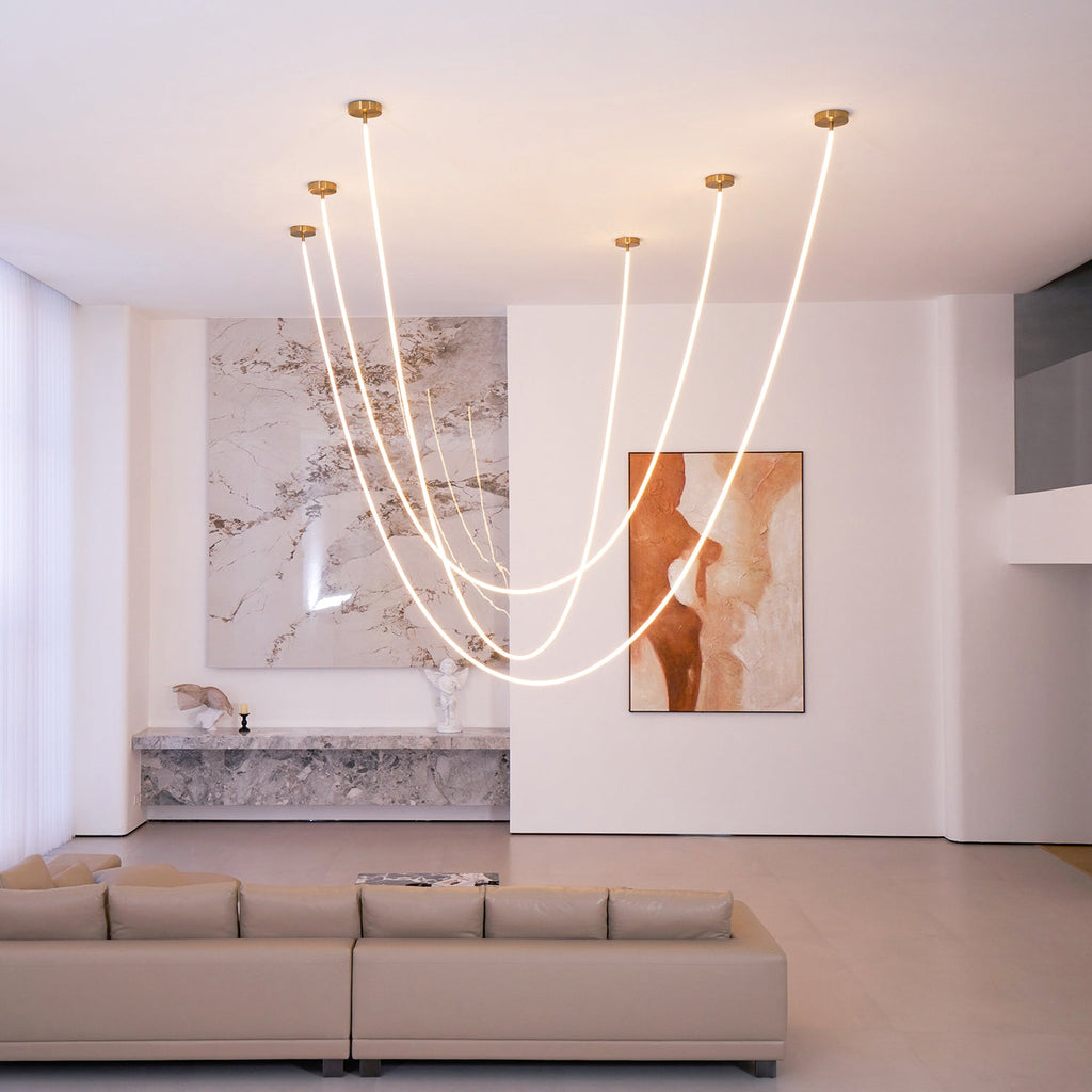 Clérachic LED rope pendants glowing from several ceiling points in a tall room, with a long taupe sofa and a rust-toned painting.