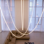 Close view of a Clérachic LED rope pendant looping in front of sheer curtains, a white column and a marble wall.