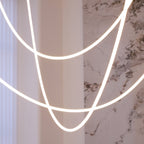 Close view of the soft, even glow along the tubes of Clérachic LED rope pendants, with a marble wall and a curtain behind.