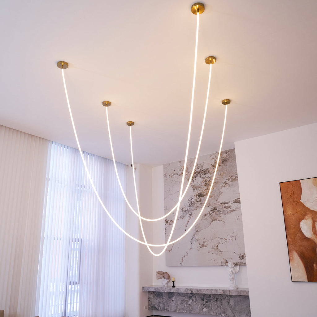 Clérachic LED rope pendants with five gold-toned plates, glowing in curves in a high white room with a marble wall and a painting.