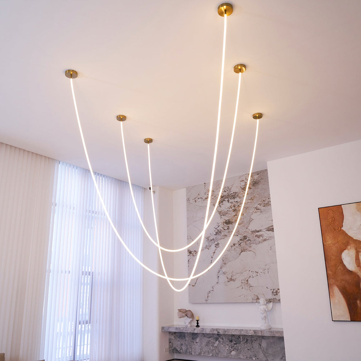 Clérachic LED rope pendants with five gold-toned plates, glowing in curves in a high white room with a marble wall and a painting.