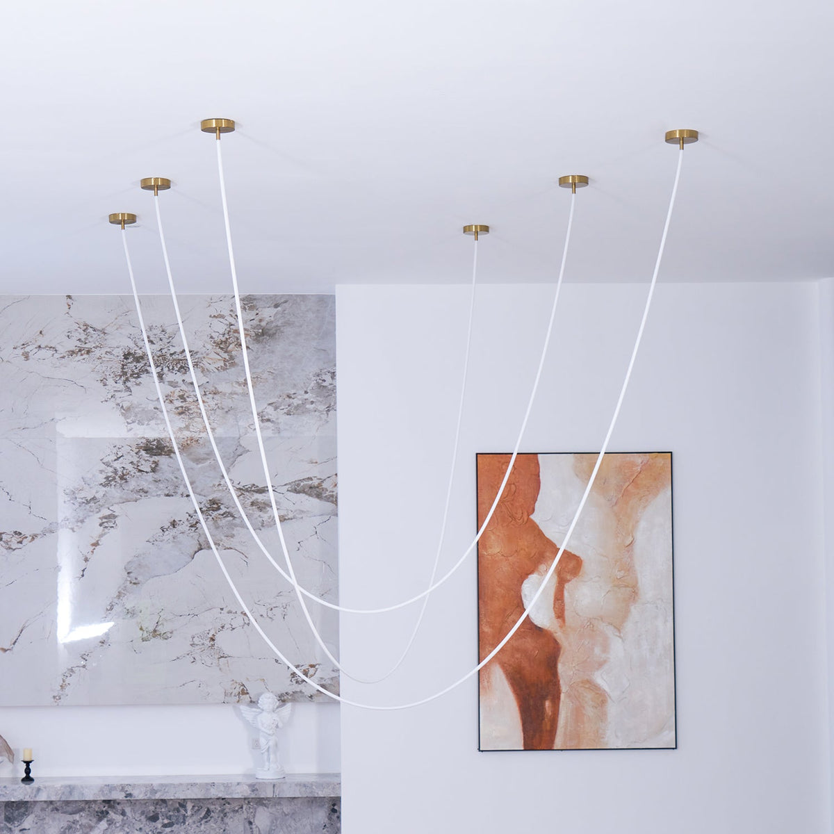 Clérachic rope pendants, switched off, in tall curves before a marble wall and a rust-and-cream painting, above a marble shelf.