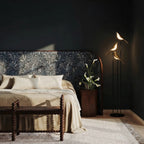 Clérachic three-head bird floor lamp glowing beside a bed with a patterned headboard against a dark wall