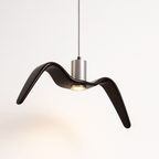 Clérachic gloss black gull-winged pendant lit warm, a small recessed spotlight on its underside beside a brushed aluminium cylinder.