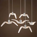 Clérachic six white gull-winged pendants of varied wing shapes on slim cords with aluminium cylinders, against a dark brown ground.