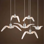Clérachic six white gull-winged pendants of varied wing shapes on slim cords with aluminium cylinders, against a dark brown ground.