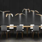 Clérachic white gull-winged pendants hung at varied heights over a long timber table, each casting a narrow downward beam.