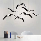 Clérachic seven gloss black gull-winged pendants at staggered heights above a white table with small ceramic and wooden objects.