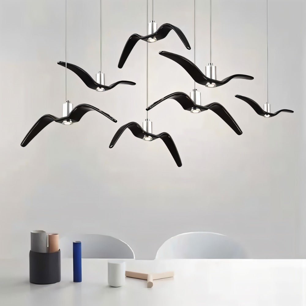 Clérachic seven gloss black gull-winged pendants at staggered heights above a white table with small ceramic and wooden objects.