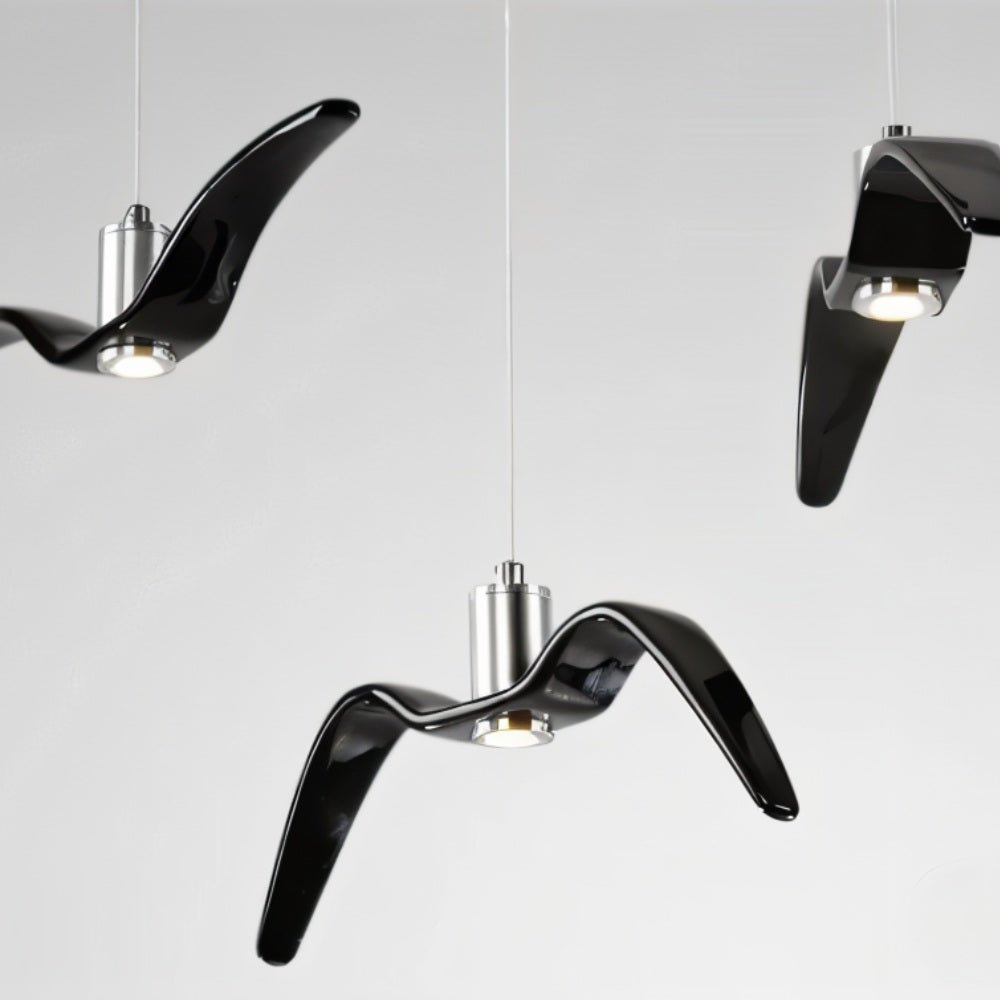 Clérachic three gloss black gull-winged pendants with aluminium cylinders and recessed warm lights, shot close on a pale grey ground.