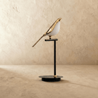 Clérachic one-head bird table lamp switched off, a polished gold bird with a white acrylic belly on a slim black stem.